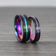 two wedding bands with rainbow and black inlays are on top of each other