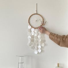 a person is holding a beaded dream catcher in front of a wall hanging on the wall