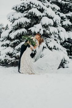 a bride and groom kissing in front of snow covered evergreen trees at their winter wedding