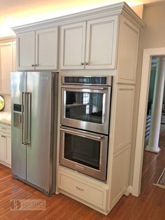 a stainless steel oven and refrigerator in a kitchen with hardwood floors, white cabinets and wood flooring