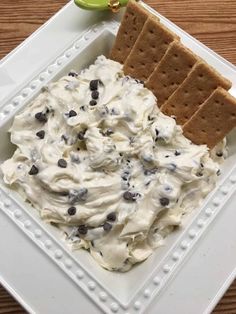 a square plate with crackers, cream and chocolate chips on it next to an apple