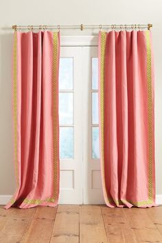 pink curtains with gold trim in front of a white wall and wooden floored area