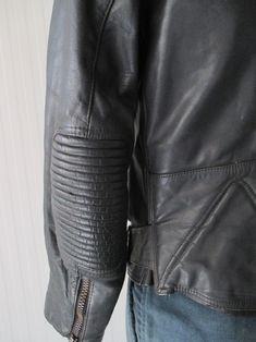 "Super 70s black biker jacket. Genuine leather. Made in Germany. It's a very solid jacket, with reinforced shouders and elbows (pic. 4-7), such as the bottom on backside (pic.8). Front black plastic zipper and mandarin collar that closes with velcro (pic.2). There are two front zipped pockets (pic.3) whose lining has to be repaired as it is unsewn. There are two other zipped pockets on waisband (pic.4-5). Two buckled straps on waistband. Quilted lining with inner pocket (pic.10). Very good condi Fitted Moto Biker Jacket, Retro Biker Jacket With Zipper For Biker Events, Fitted Biker Jacket For Urban Adventures, Vintage Biker Jacket For Winter Urban Adventures, Fitted Moto Leather Jacket For Motorcycling, Fitted Moto Biker Jacket For Motorcycling, Fitted Biker Jacket For Motorcycling, Fitted Cafe Racer Biker Jacket For Motorcycling, Retro Leather Biker Jacket With Zipper Closure