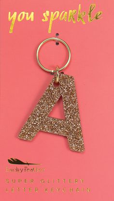 a gold glitter letter keychain on a pink card with the words you sparkle