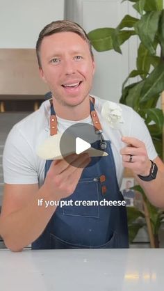 a man in an apron is holding up some cream cheese and smiling at the camera