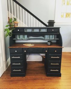 a black desk with drawers underneath a stair case and potted plant next to it