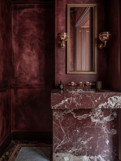 a bathroom with red walls, marble counter and vanity in the corner is an antique mirror