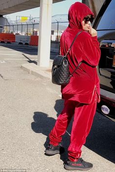 a woman in a red outfit is talking on her cell phone while standing next to a car