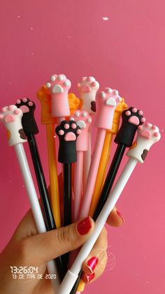 a hand holding five different colored pens with paw prints on them and one is black, the other is pink