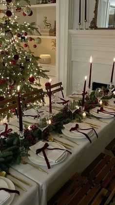 a christmas table setting with candles, plates and napkins on the long dining table