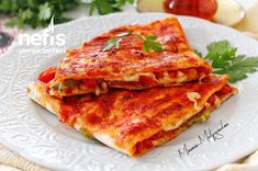 two pieces of lasagna on a white plate with parsley sprig