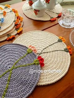 crocheted placemats with flowers on them are sitting on a wooden table