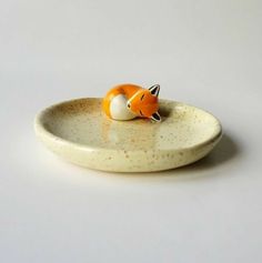 an orange and white ceramic fox figurine sitting on a plate with its tail curled up