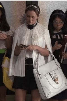 a woman in white jacket and black skirt holding a purse next to other women with cell phones