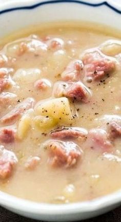 a white bowl filled with soup and meat on top of a wooden table next to a spoon