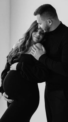 a pregnant couple cuddles in their black and white photo session at the studio