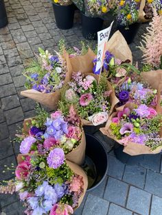 several buckets filled with lots of flowers on top of a brick floor next to potted plants