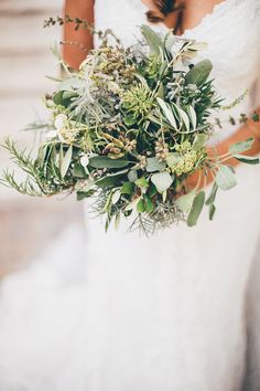 a woman in a white dress holding a bouquet of flowers and greenery on her wedding day