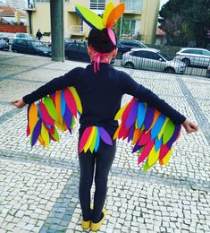 a woman in black shirt with colorful wings on brick road next to building and cars