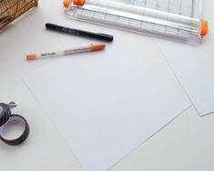 a pair of scissors, tape and some other items on a white table with orange trimmings