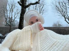 a woman wearing a white knitted coat and scarf covers her face from the cold