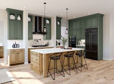 a large kitchen with green cabinets and white counter tops, black bar stools, and wooden flooring