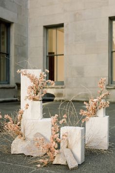 four cement blocks with flowers growing out of them in front of a large stone building