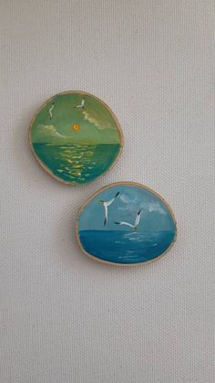 two small plates with seagulls flying over the ocean on white canvass, one painted in blue and green