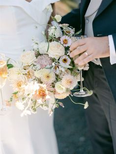 the bride and groom are holding champagne glasses with their bouquets in front of them