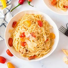 pasta with tomatoes and cheese in a white bowl on a table next to other food