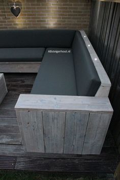 an outdoor seating area made out of wood and black leather cushions, with brick wall in the background