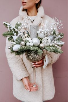 a woman wearing a fur coat holding a wine glass filled with greenery and ornaments