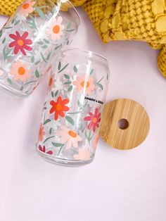 two clear tumblers with flowers painted on them next to a yellow sweater and wooden object