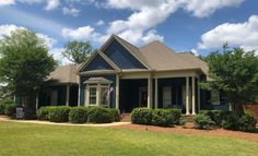 a blue house with two front porches and bushes in the front yard on a sunny day