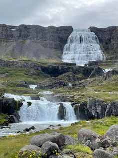 a large waterfall in the middle of a grassy area with rocks and grass around it