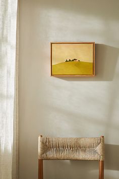 a painting hangs on the wall next to a wooden bench in front of a window