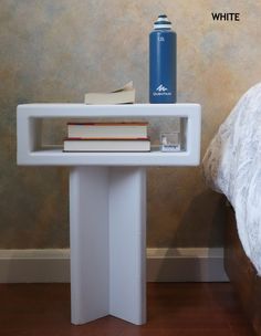 a white table with books and a blue water bottle on it next to a bed