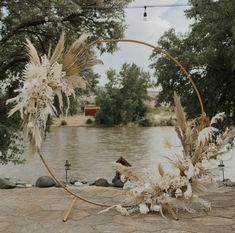 an outdoor wedding ceremony setup with pamodia flowers and feathers on the hoop by the water