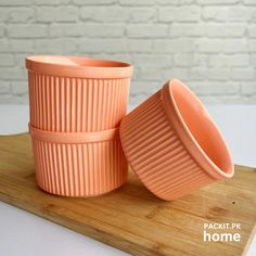 two orange cups sitting on top of a wooden cutting board