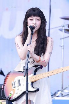 a woman singing into a microphone while holding a guitar in front of her and an electric guitar behind her