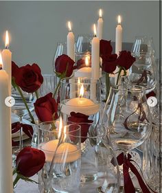 a table topped with lots of candles and vases filled with red rose's