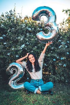 a woman sitting on the ground holding up two silver balloons in front of her face