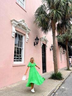 a woman in a green dress is walking down the sidewalk near a pink building with palm trees