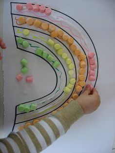 a child's hands holding up a paper plate with candy on it and the shape of a rainbow