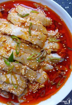 a white bowl filled with meat covered in sauce and garnished with sesame seeds