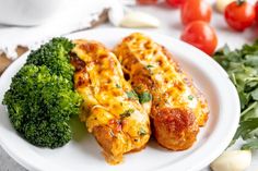 two pieces of chicken on a plate with broccoli and tomatoes next to it