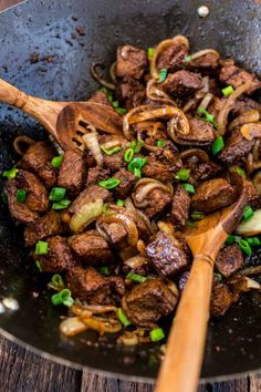 beef and onions cooking in a skillet with wooden spoons on the side, ready to be eaten