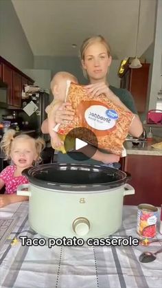 a woman holding a baby while standing next to a crock pot