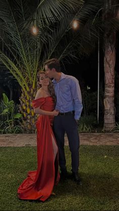 a man and woman standing next to each other in front of a palm tree at night