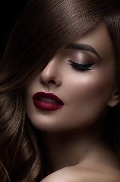 a woman with long brown hair and red lipstick on her face, wearing dark makeup